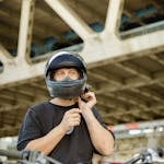 A motorcyclist fastens his helmet beneath an urban overpass, ready for adventure.