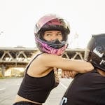 A woman in a helmet sitting on a motorcycle riding through an urban area.